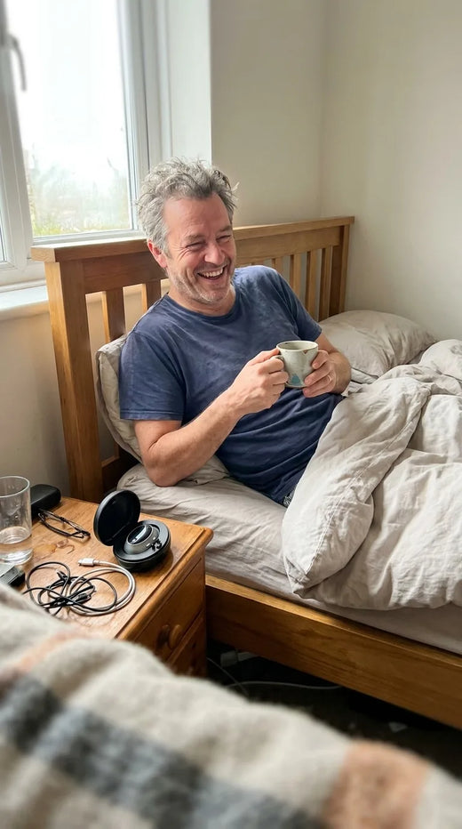 Man laughing in bed with a morning coffee, the Hushlea Pro case open on the nightstand