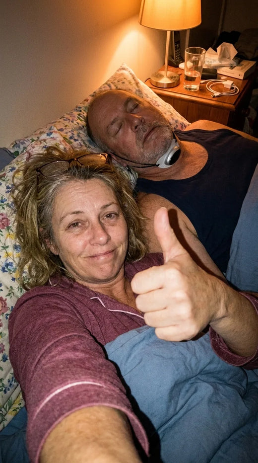 Woman giving a thumbs up in bed at night while her husband sleeps quietly wearing Hushlea Pro under his chin